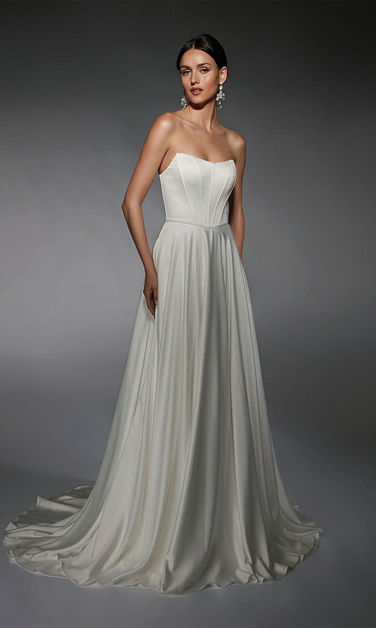 A woman in the Alyce 7110 long white dress, featuring a strapless fitted bodice and flowing skirt, stands against a plain dark background.